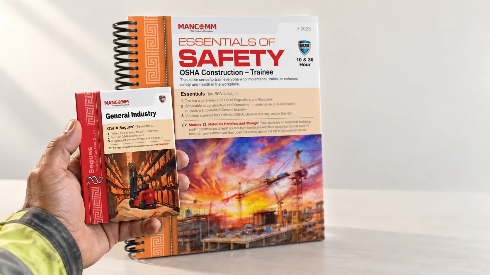 A hand holding the pocket-sized HEART workbook in front of the Essentials of Safety manual